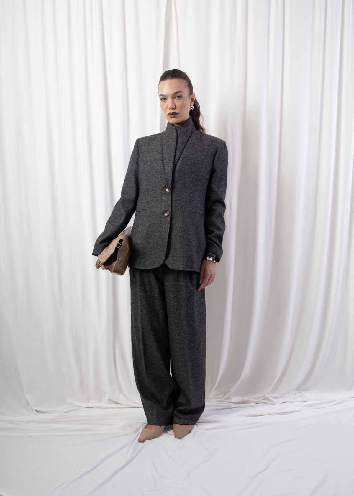 Model wearing a tailored blazer with notched lapels, two-button front closure, and welt pockets, styled indoors against a white backdrop.