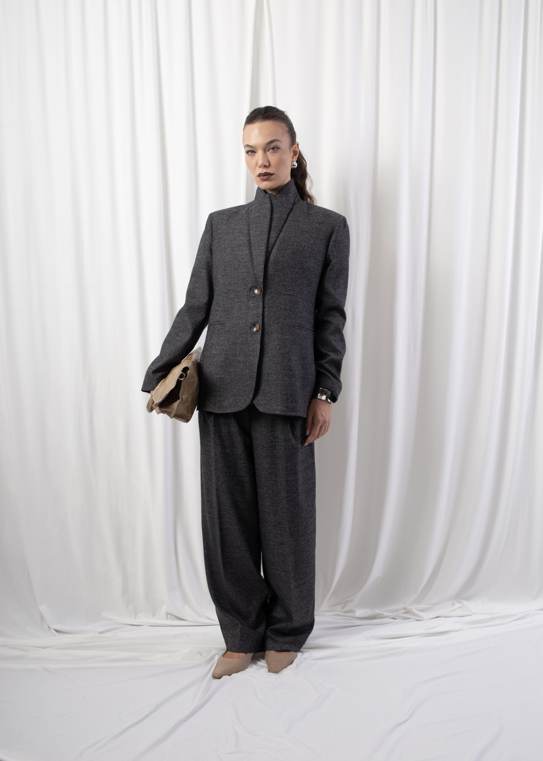 Model wearing a tailored blazer with notched lapels, two-button front closure, and welt pockets, styled indoors against a white backdrop.