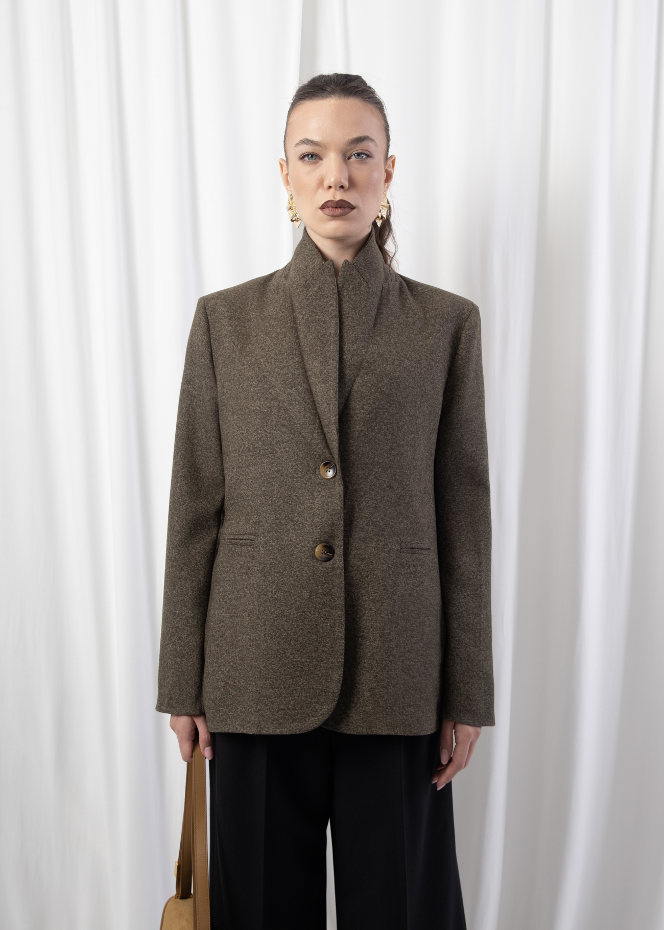 Model wearing a green tailored blazer with notched lapels, two-button front closure, and welt pockets, styled indoors against a white backdrop.