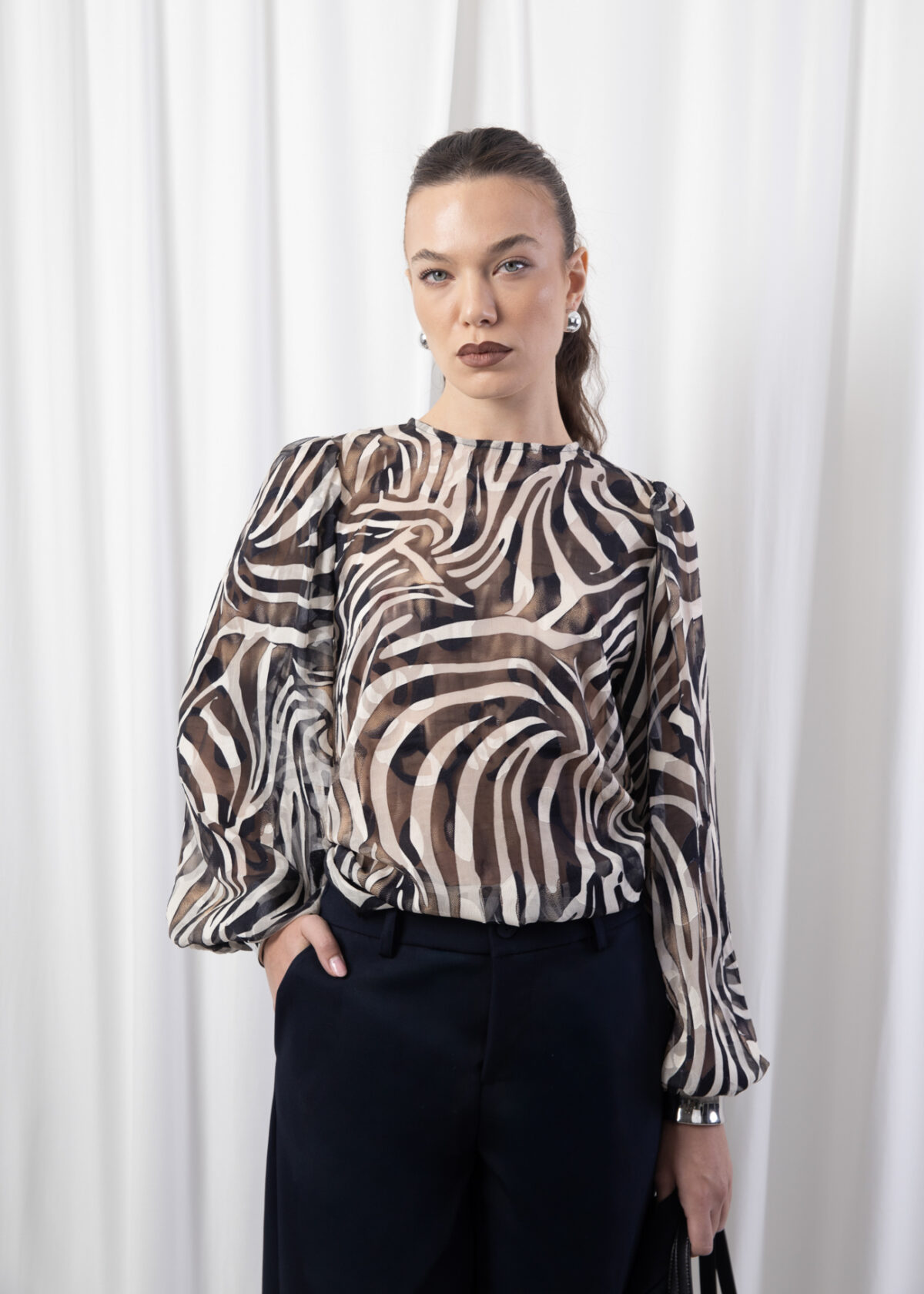 Model wearing a sheer printed blouse with round neckline, puff sleeves, and back keyhole button closure.