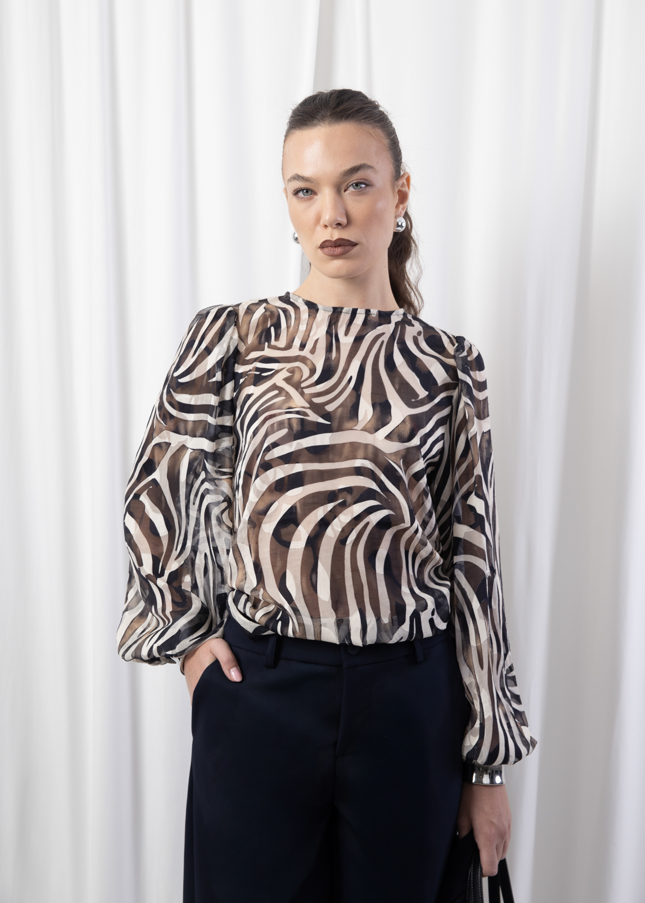 Model wearing a sheer printed blouse with round neckline, puff sleeves, and back keyhole button closure.