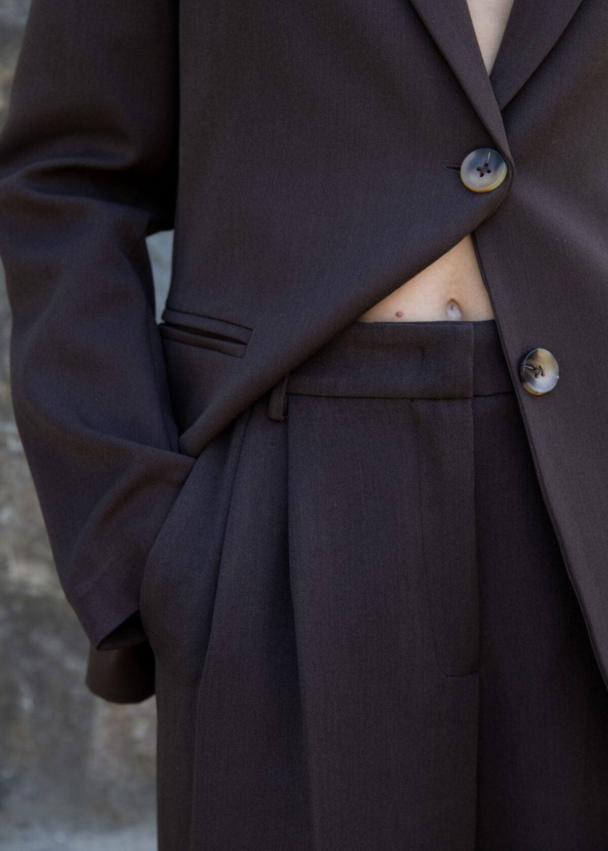 Model wearing high-rise wide-leg trousers with front pleats, back flap pockets, and pressed crease, styled with a matching blazer in outdoor setting.