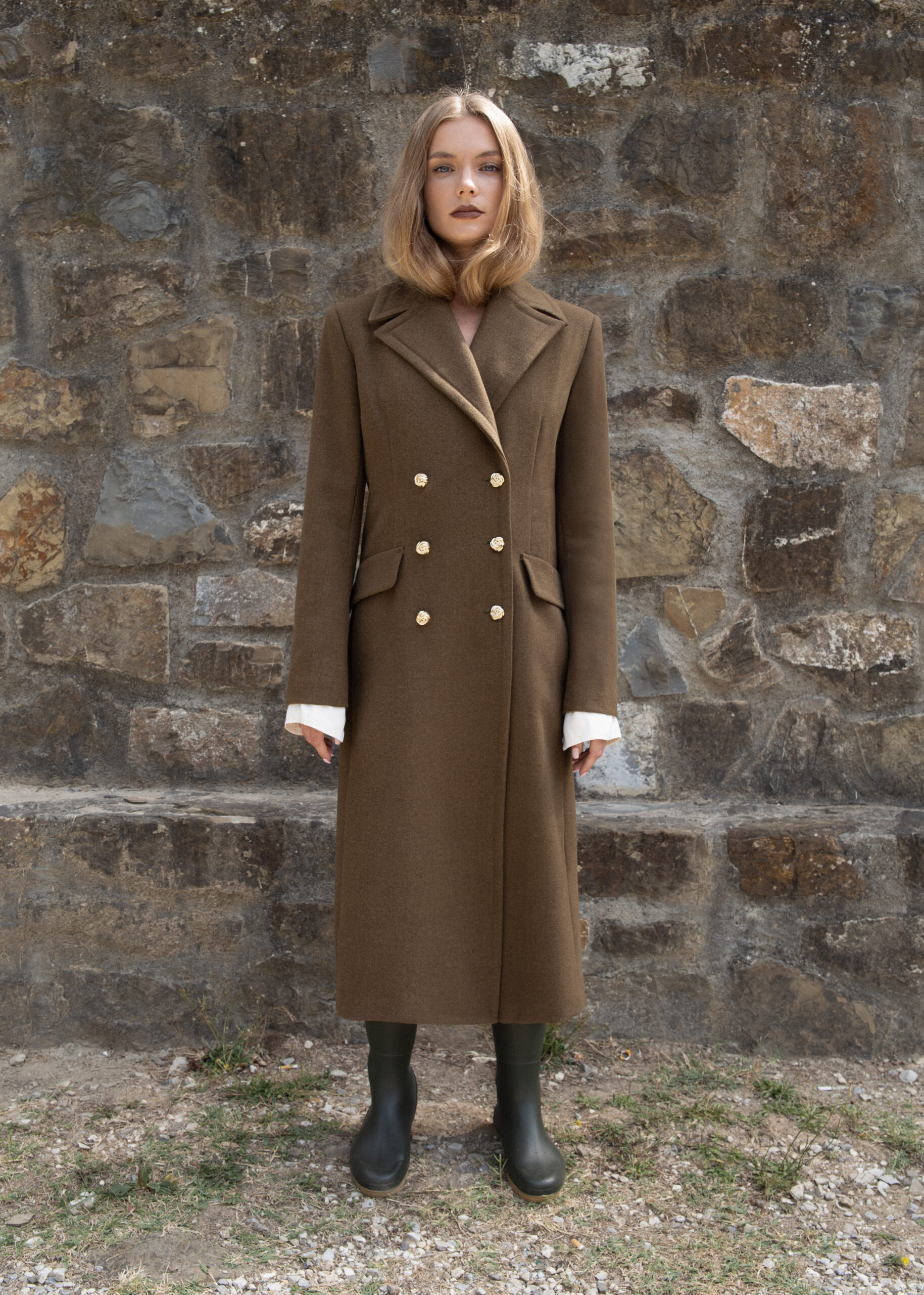 Double-breasted long wool-blend coat with gold buttons, peak lapels, and flap pockets, tailored in a structured silhouette.